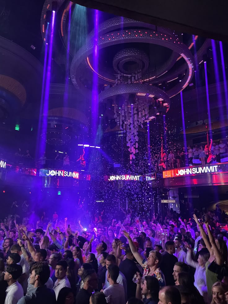 a large group of people at a party with purple lights and confetti on the ceiling