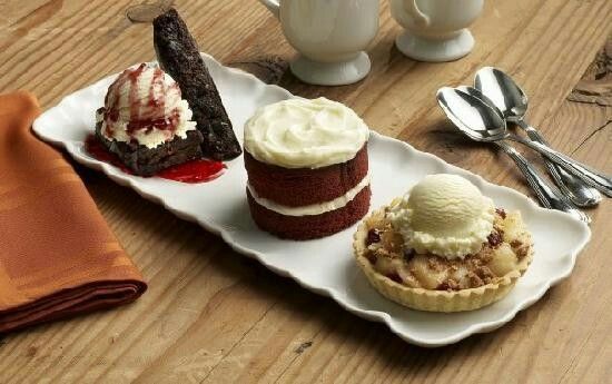 three pastries on a white plate with spoons and coffee mug in the background