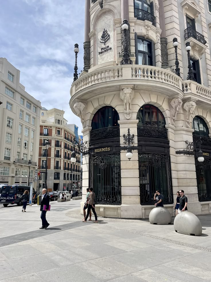 some people are walking around in front of a building with many windows and balconies