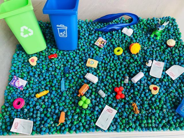 there are many toys in the sand on this beach mat, and one has a blue trash can