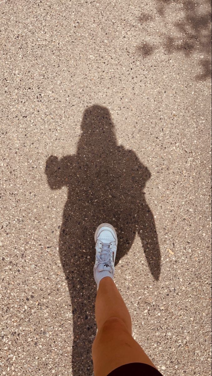 the shadow of a person's leg and foot on asphalt with a blue shoe