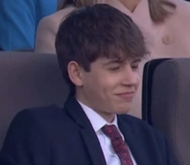 a young man wearing a suit and tie sitting in front of an audience at a sporting event