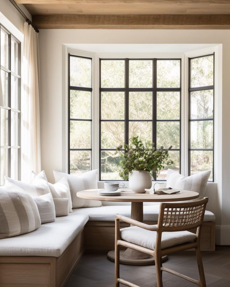 a table with two chairs and a bench in front of a window that has large windows