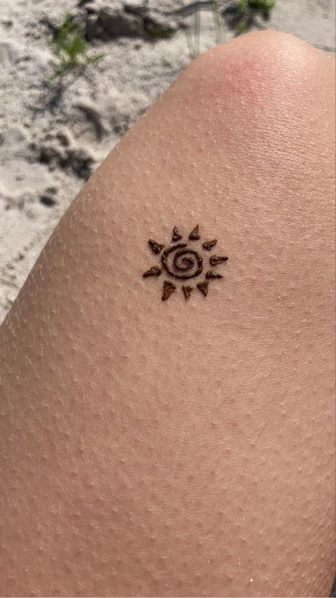 a sun tattoo on the back of a person's left arm, with sand in the background