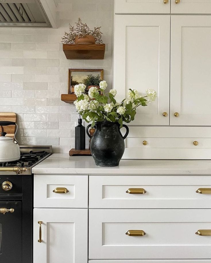 a kitchen with white cabinets and gold pulls on the doors, black stove top oven