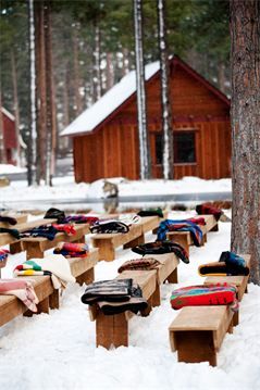 many pairs of shoes are lined up on benches in the snow near a log cabin