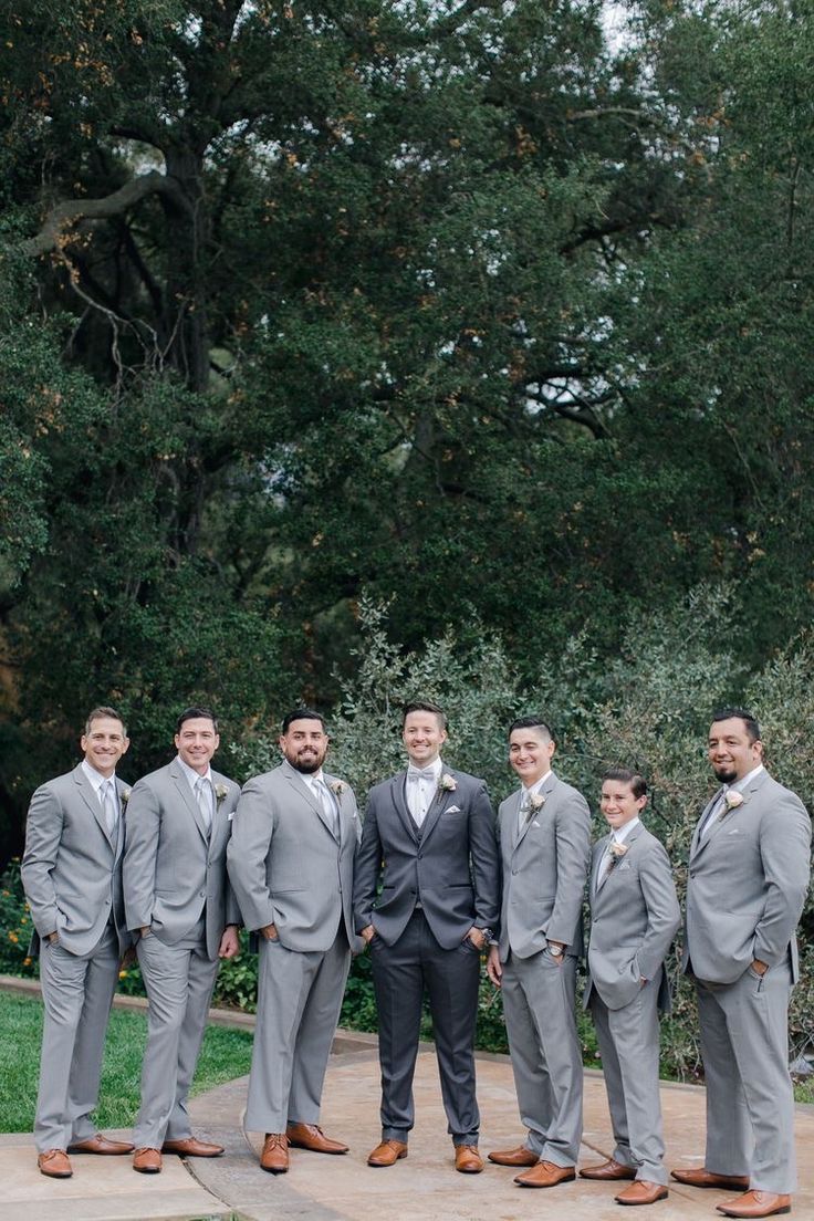 a group of men standing next to each other in front of some green trees and bushes