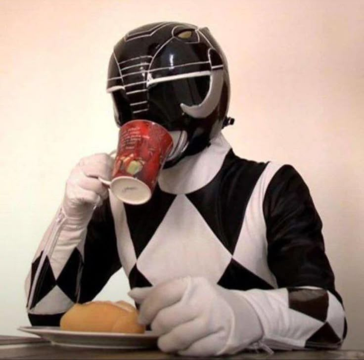 a person in a black and white suit is drinking from a can while sitting at a table