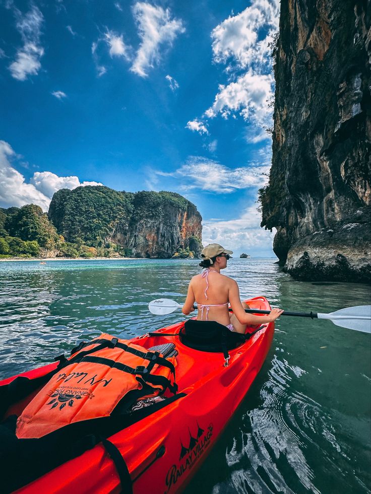 a woman is paddling her kayak in the water near an island with cliffs