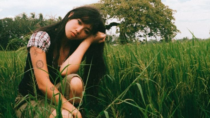 a woman sitting in tall grass with her hand on her head