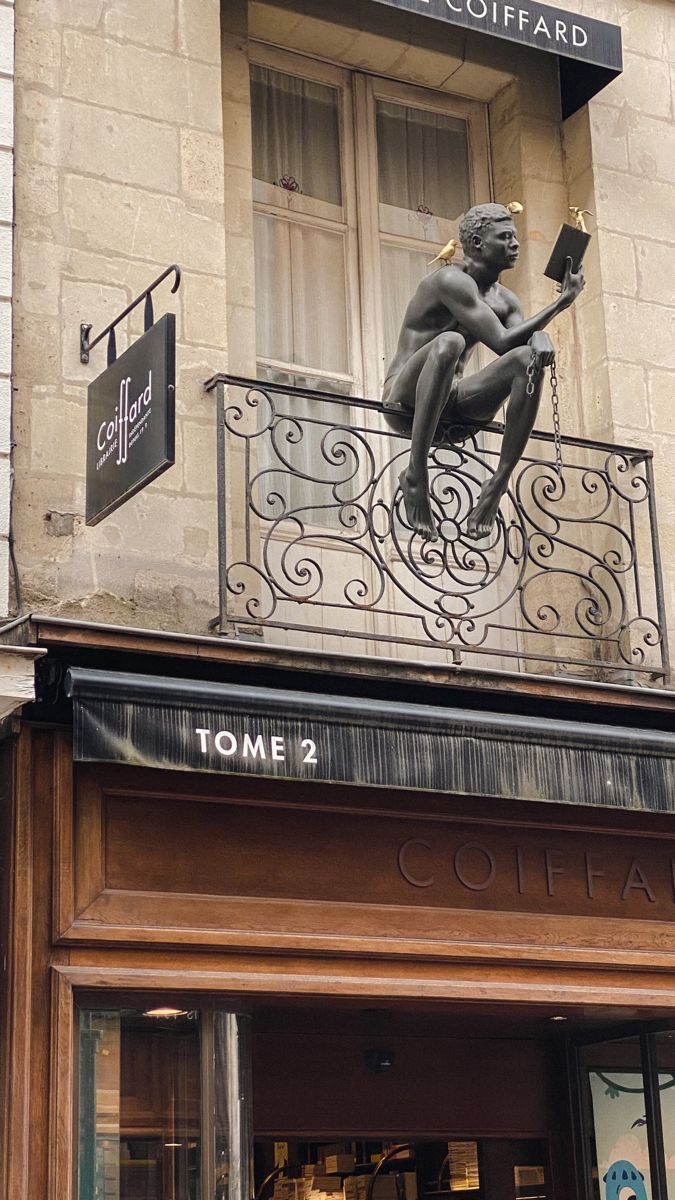 a statue is sitting on the balcony of a building with an open door and sign above it