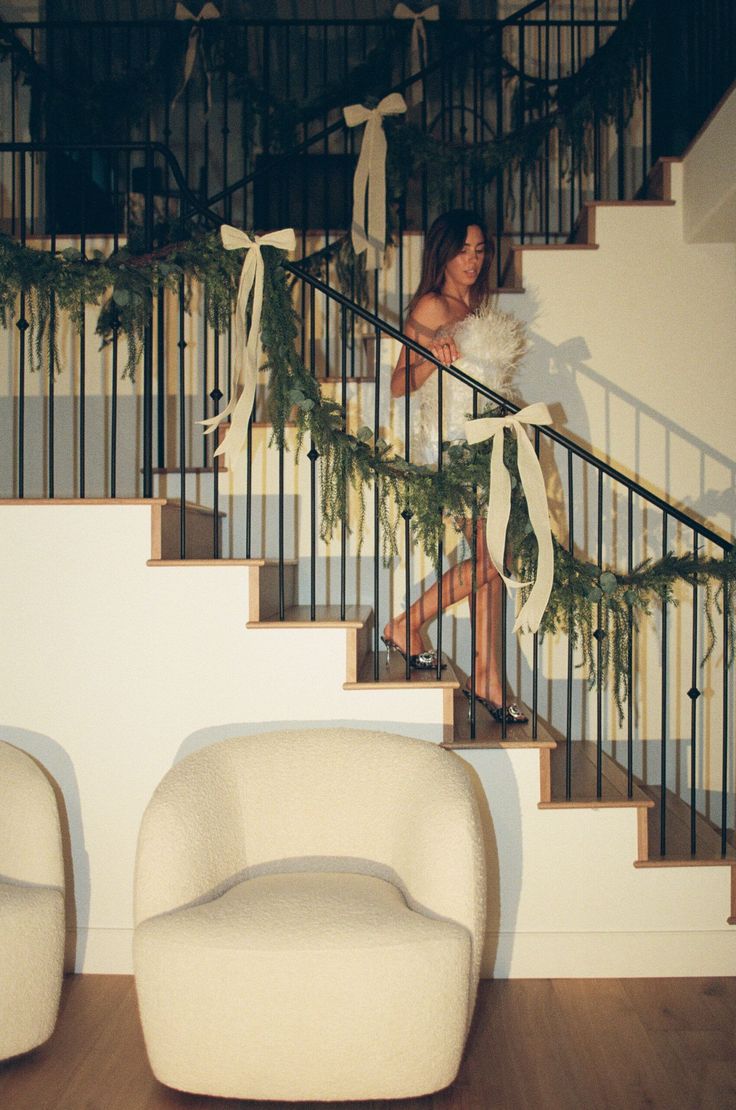 a woman is walking down the stairs with christmas garland on her handrail and dress