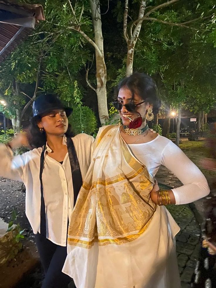 two women standing next to each other in front of a tree at night with lights on