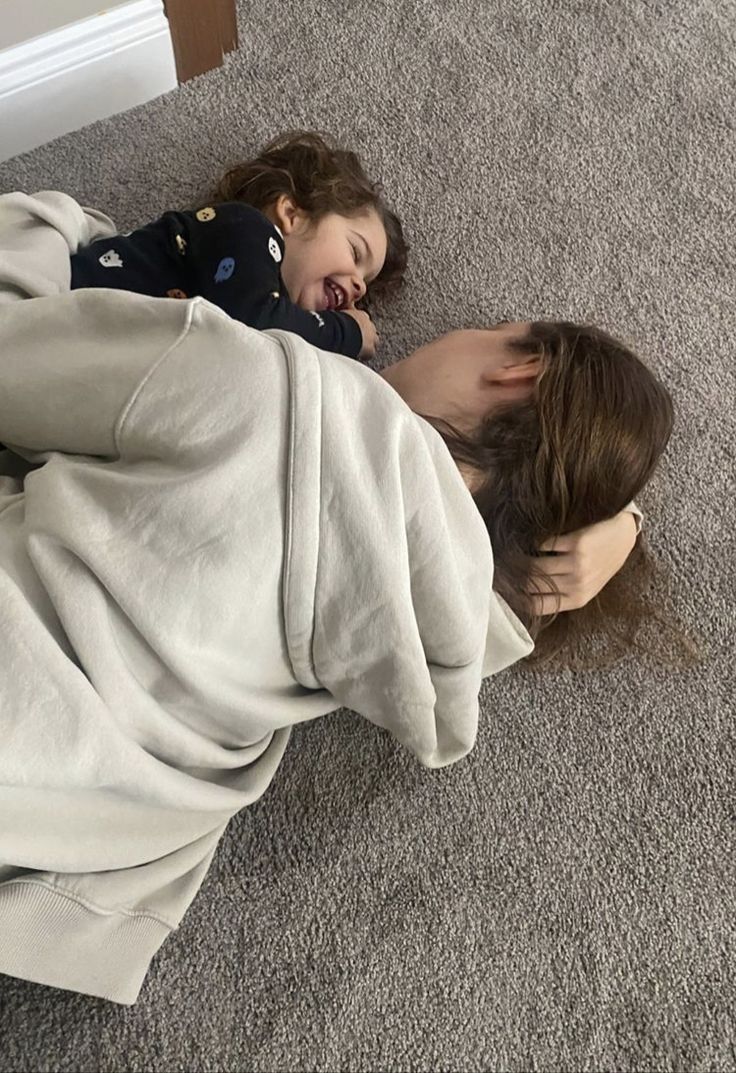 a woman and child laying on the floor under a blanket