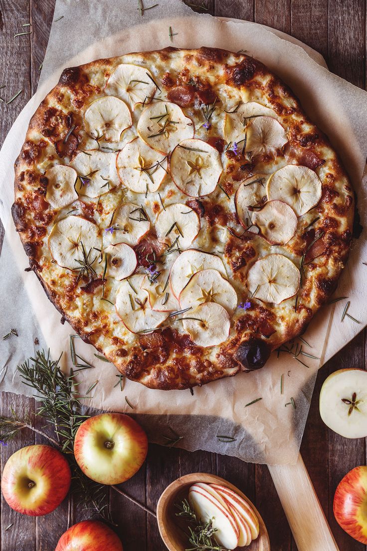 an apple and rosemary pizza with sliced apples on the side, next to it's serving utensils