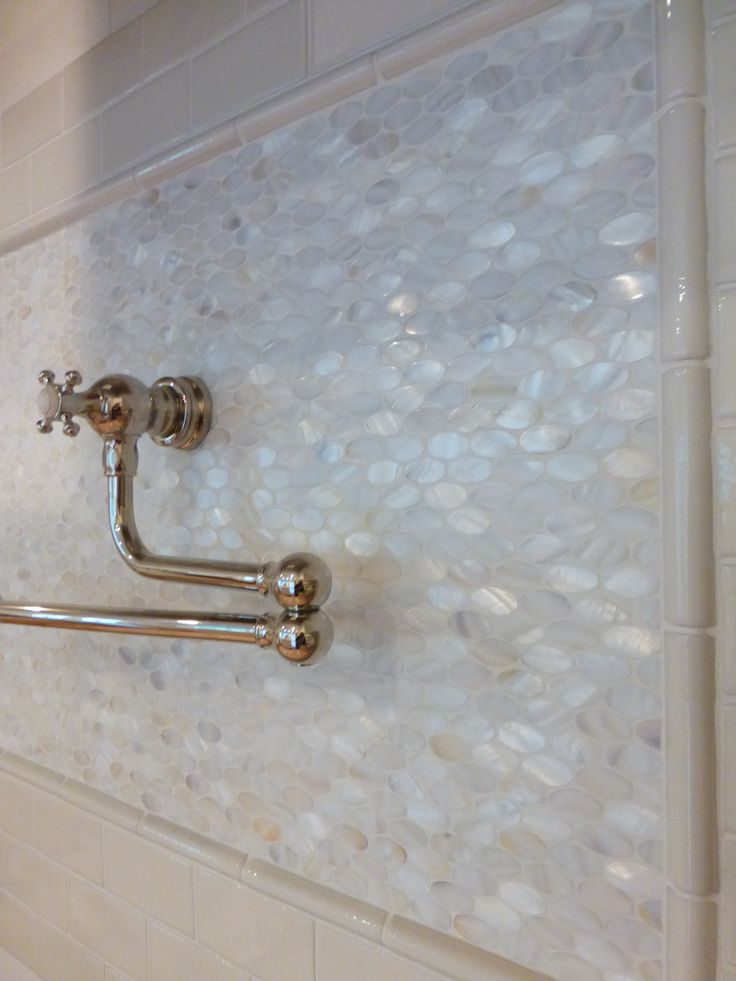 a bathroom with white tile and gold faucets on the shower wall next to toilet paper dispenser