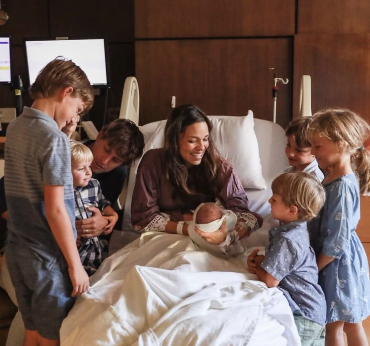 a group of children standing around a woman in a hospital bed with a baby on her lap