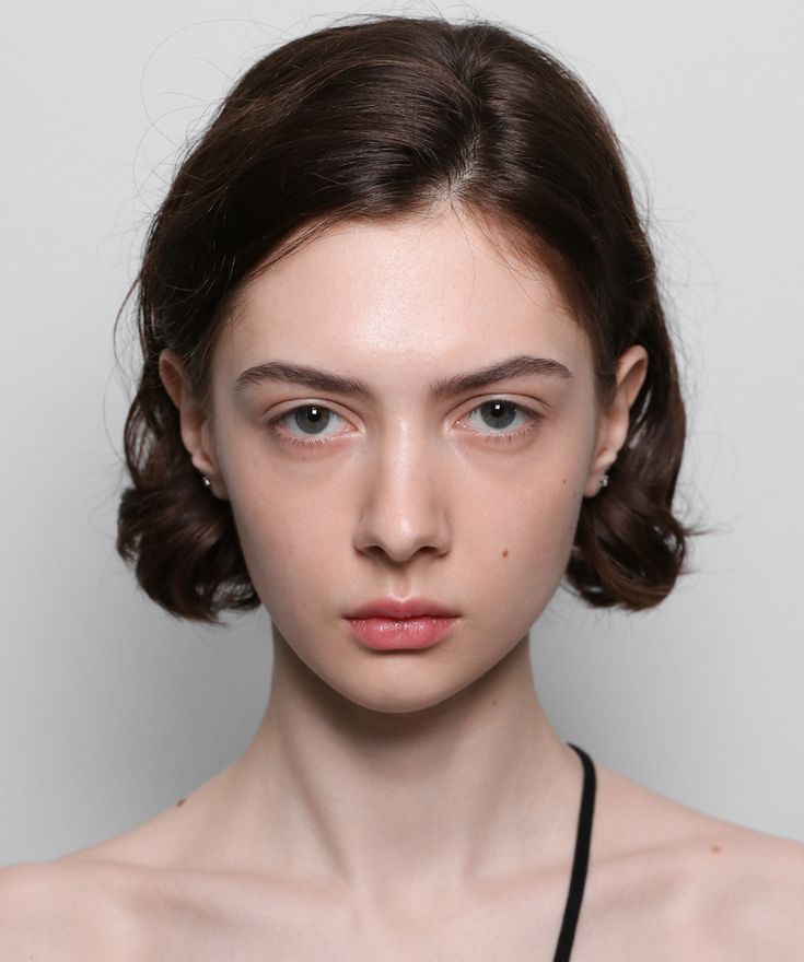 a woman with dark brown hair and blue eyes wearing a black bra over a white background