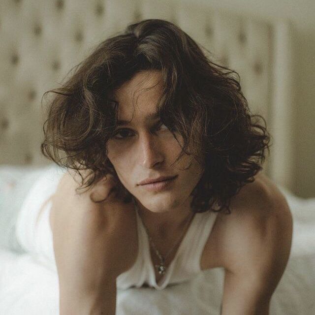 a man with long hair sitting on a bed