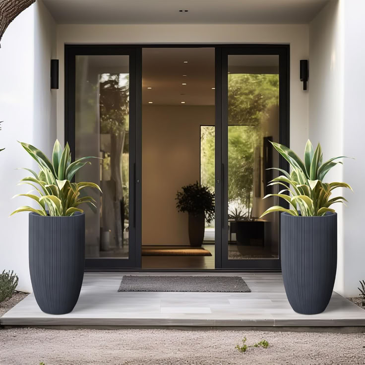 two large planters on the outside of a door way with plants in front of them