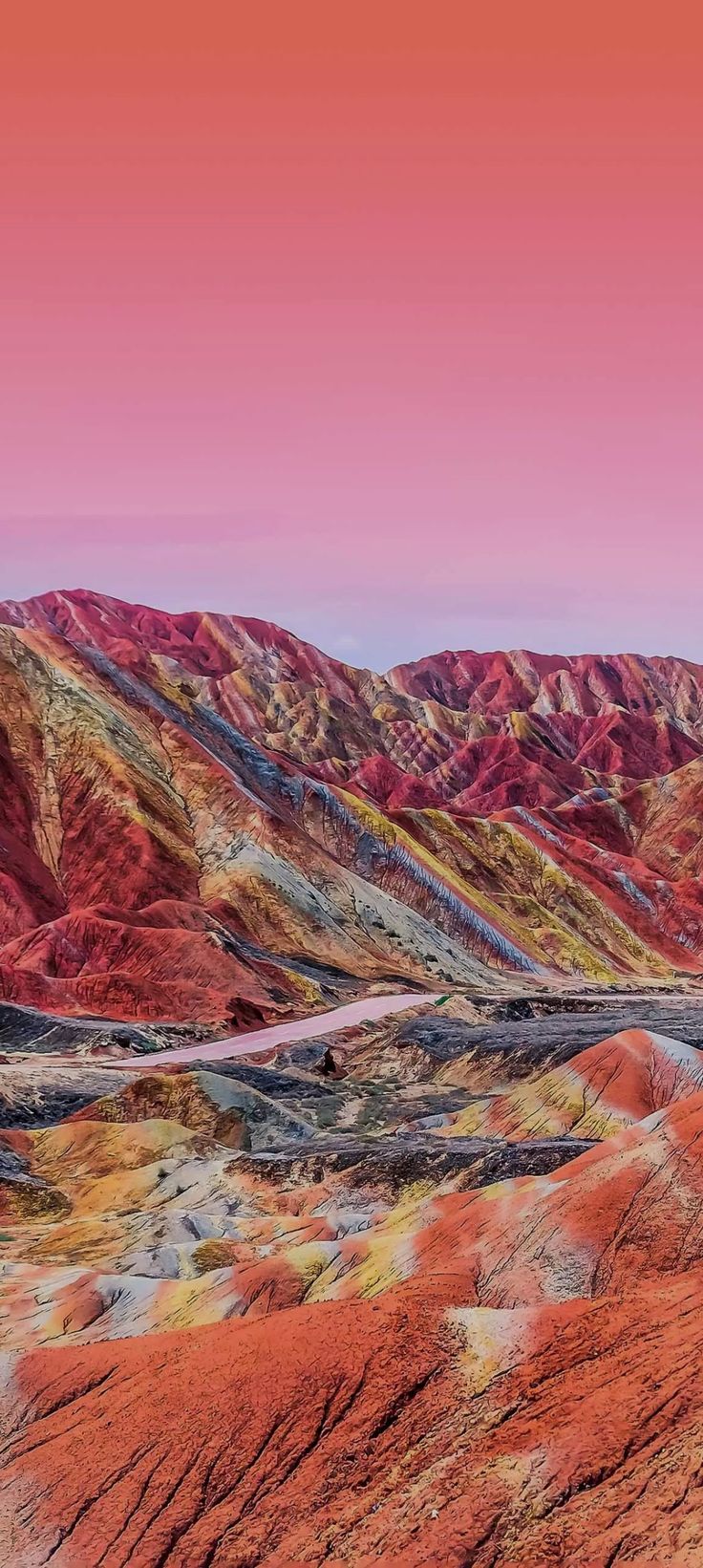 the mountains are covered in red, orange and yellow colors with a road going through them