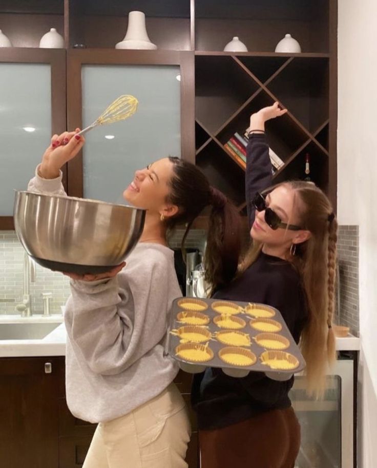 two young women are cooking cookies in the kitchen and one is holding a spatula