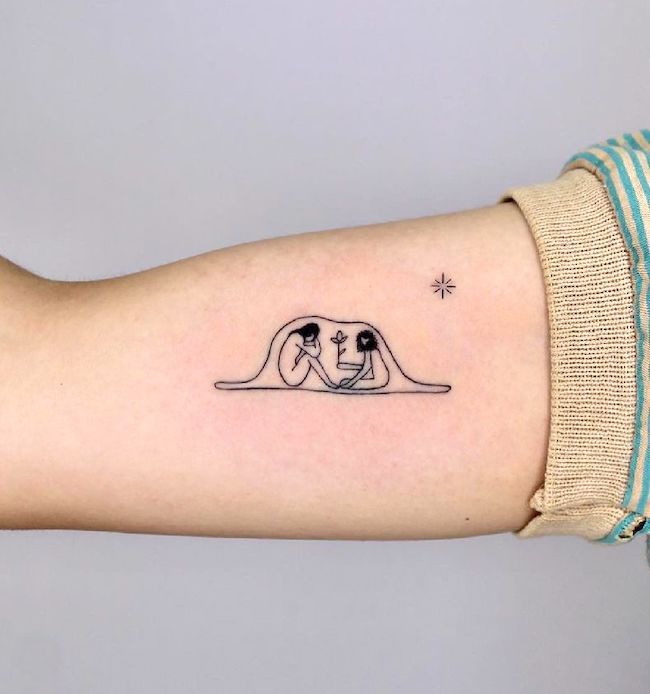 a woman's arm with a small tattoo of two people laying on the ground