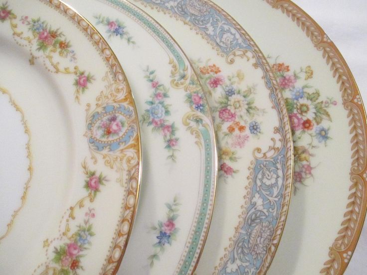 four plates with floral designs on them sitting next to each other in front of a white tablecloth