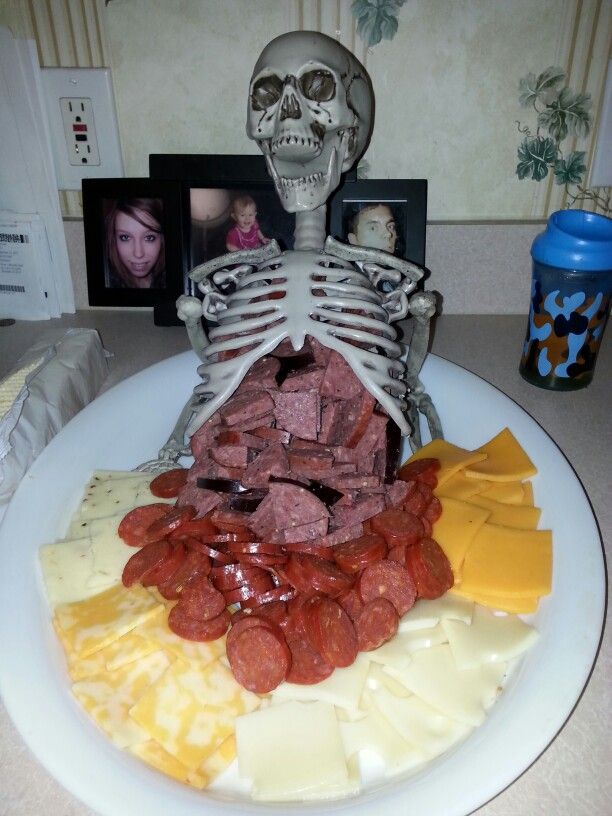 a skeleton sitting on top of a white plate filled with cheese and meat