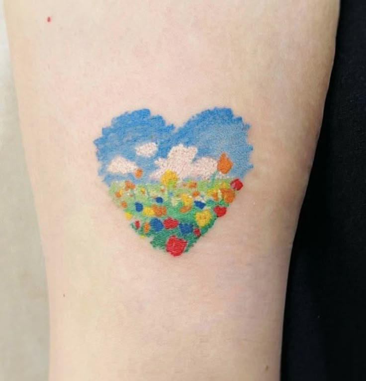 a small heart shaped tattoo on the back of a woman's left arm with flowers and clouds painted on it