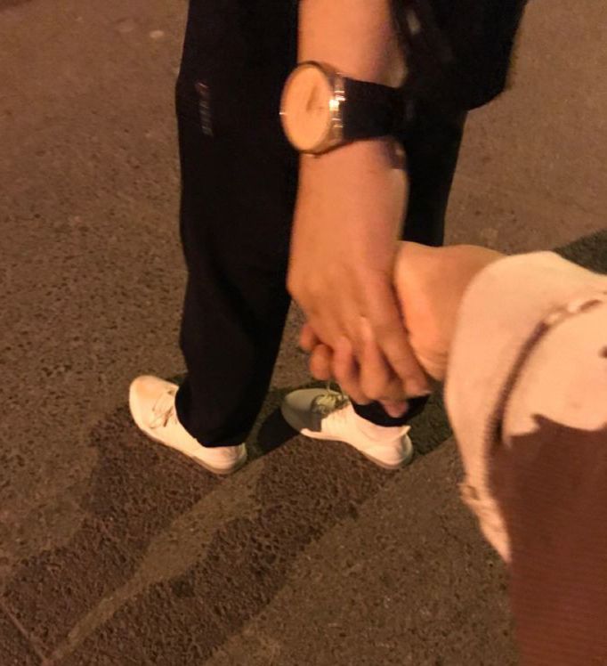 two people holding hands while walking down the street at night with their feet on another person's leg