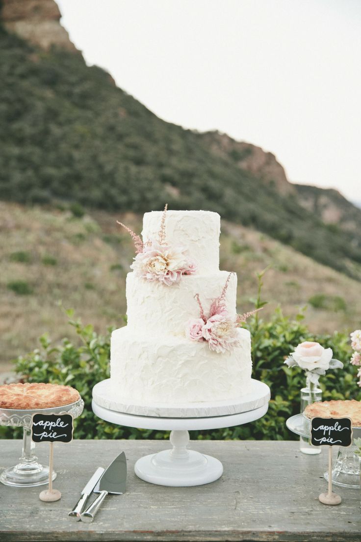 a white wedding cake sitting on top of a wooden table next to other desserts