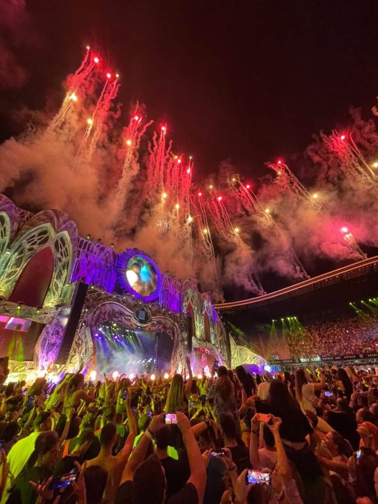 fireworks are lit up in the night sky above an outdoor concert venue with people taking pictures