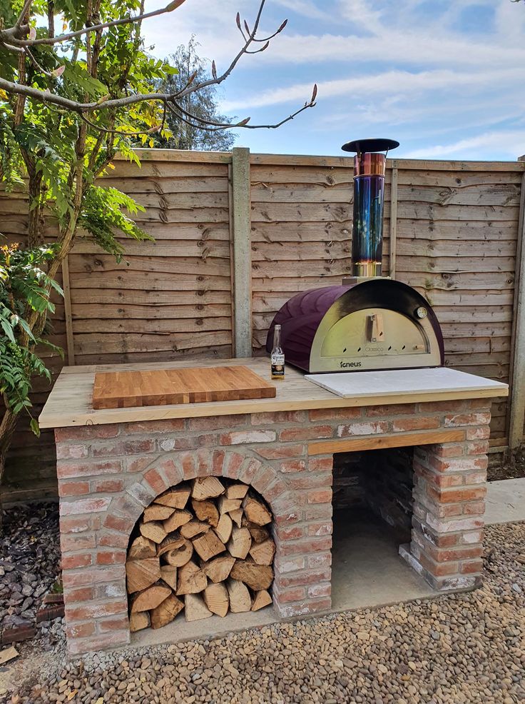 an outdoor pizza oven with firewood in the front and side area next to it