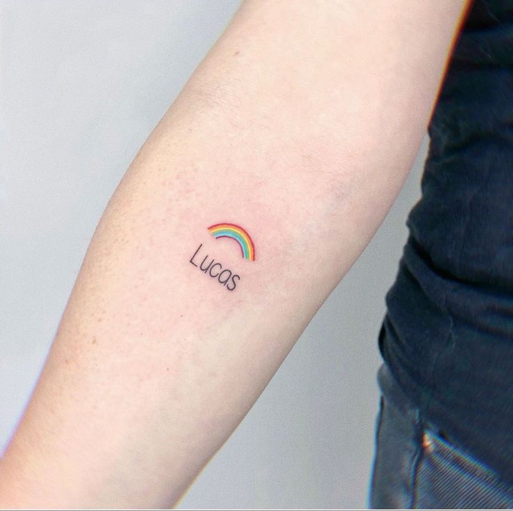 a woman's arm with a small tattoo on it that says lucas and a rainbow