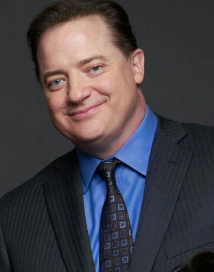 a man in a suit and tie smiling at the camera while wearing a blue shirt