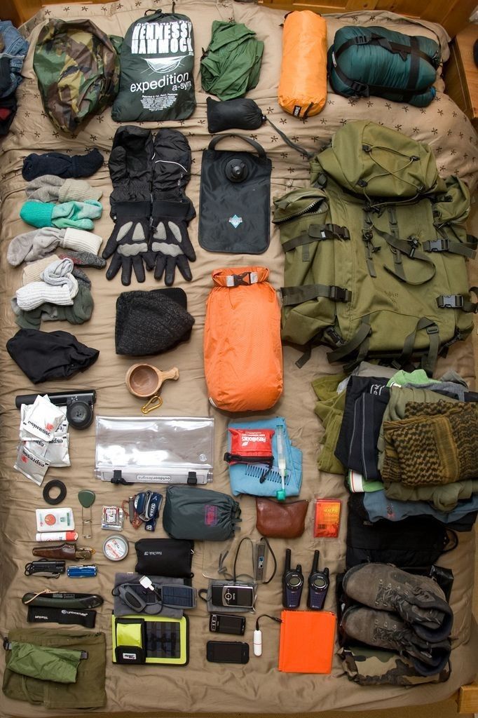 an assortment of items laid out on top of a bed in a box, including gloves and backpacks