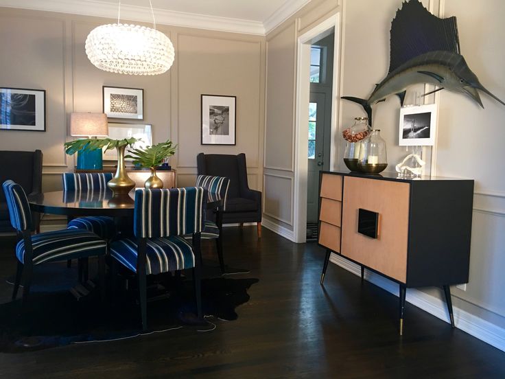 a dining room table with blue chairs and pictures on the wall behind it, along with a shark head mounted to the wall