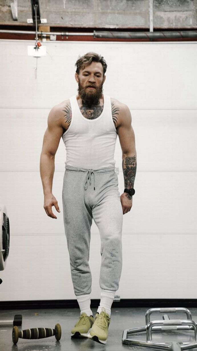 a man standing in front of a garage door wearing sweatpants and yellow shoes with his hands on his hips