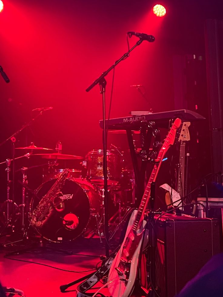 the band is performing on stage in front of microphones and drums with red lighting