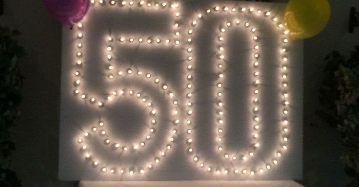 a lighted sign that says 50 with balloons on it in front of a party table