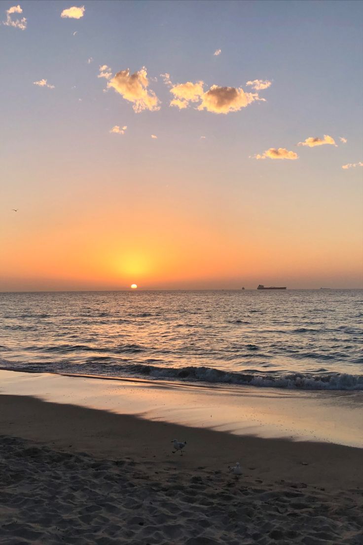 the sun is setting over the ocean with clouds in the sky and on the beach