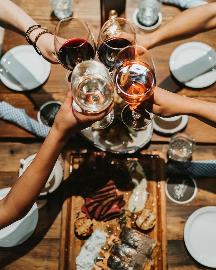 several people are toasting with wine glasses at a table full of food and drinks