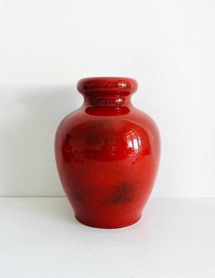 a red vase sitting on top of a white table