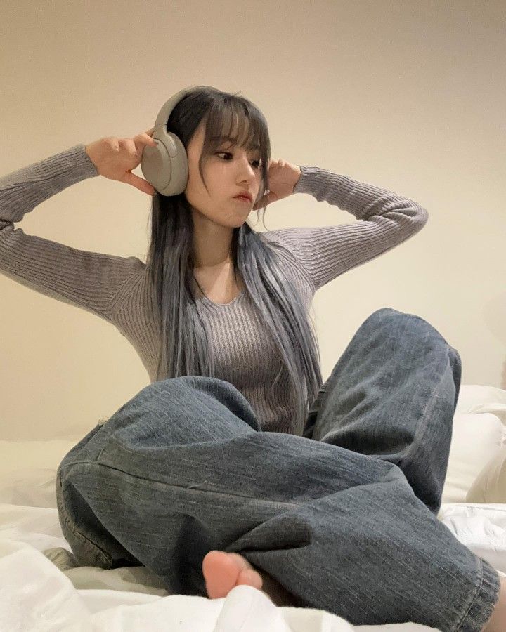 a woman sitting on top of a bed holding headphones to her ears with both hands