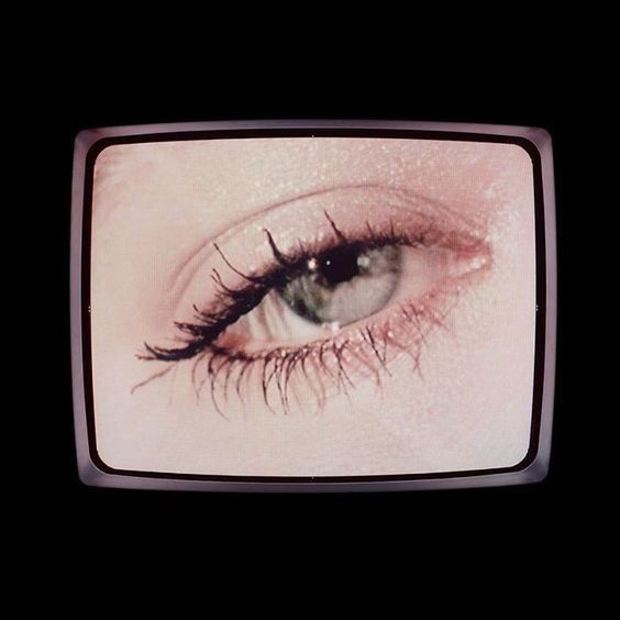 an eye with long lashes is shown on a television screen in the dark, looking straight ahead