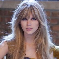 a woman with long blonde hair standing in front of a brick wall and looking at the camera