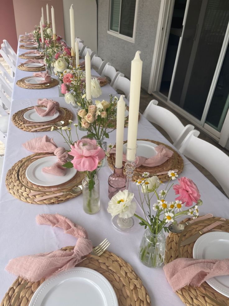 the table is set with pink and white flowers in vases, plates and napkins