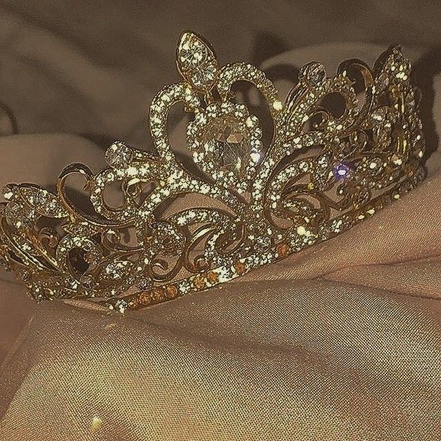 a gold tiara sitting on top of a pink cloth next to a white pillow