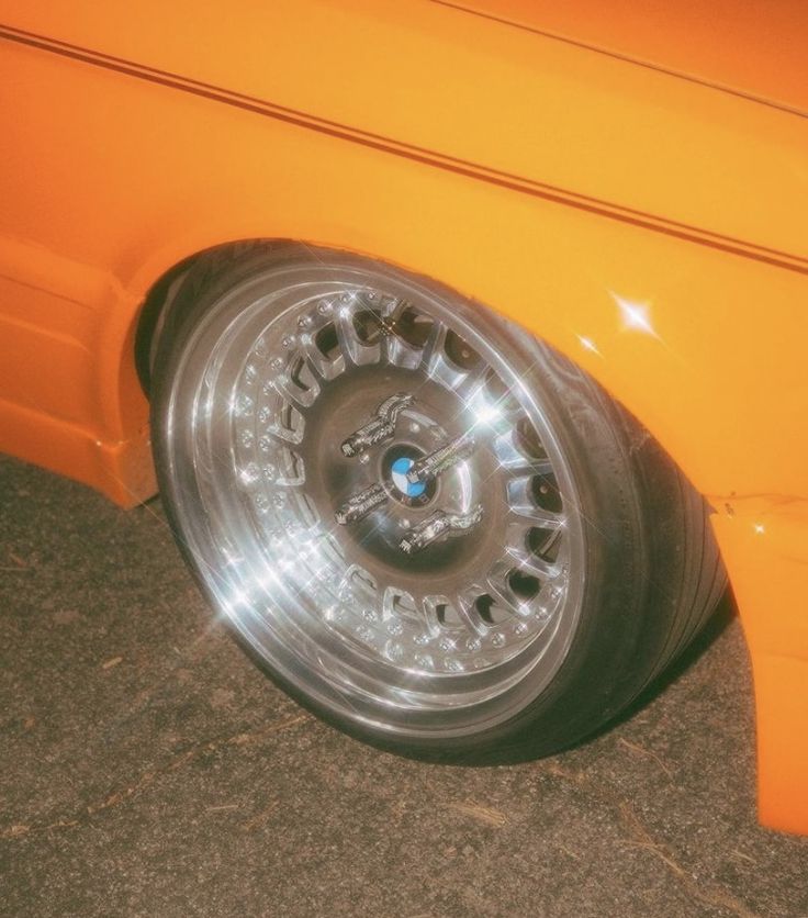 an orange car with chrome rims parked on the street